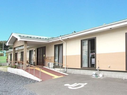 平屋建ての建物。手すり付きのスロープが付き、障害者マークが付いた駐車スペースがある。