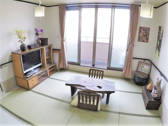 畳の部屋に小さなテーブルと座椅子テレビなどが置いてある広めの和室の様子