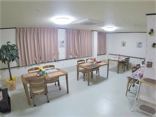 広めのホールにいすと机が並んでいる様子。カーテンがかかっている窓がある様子
