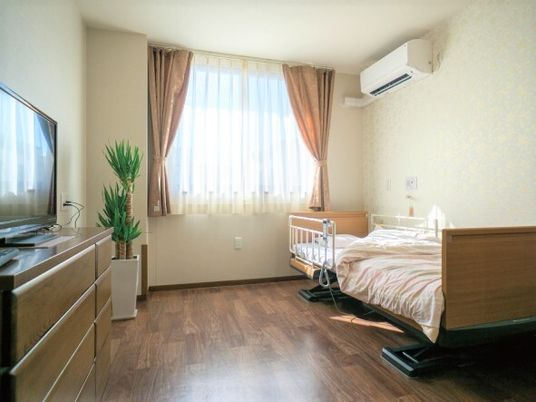 居室はフローリングでエアコンやテレビ、寝具付きのベッドや観葉植物も置かれている。