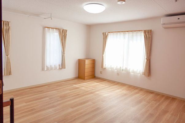 大きな窓が付いた居室。エアコンやたんすが付き、シンプルなフローリングの部屋。