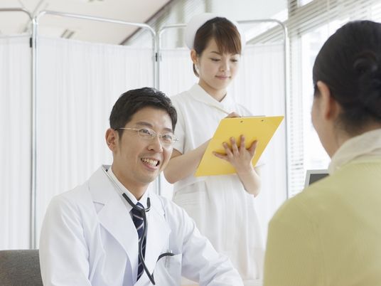 患者と何かについて話している医師。後ろには看護師が付いているのが分かる