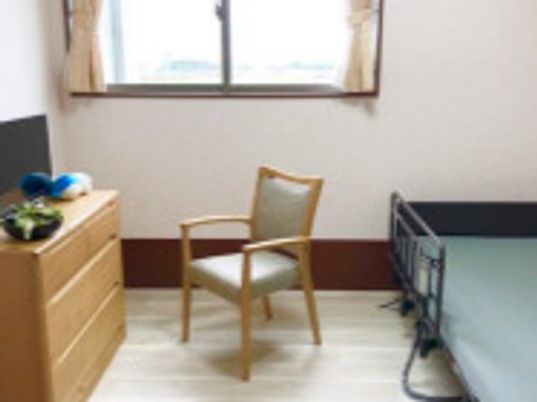 フローリングの部屋には介護ベッドやいす、タンス、テレビ、大きな窓が付いている。
