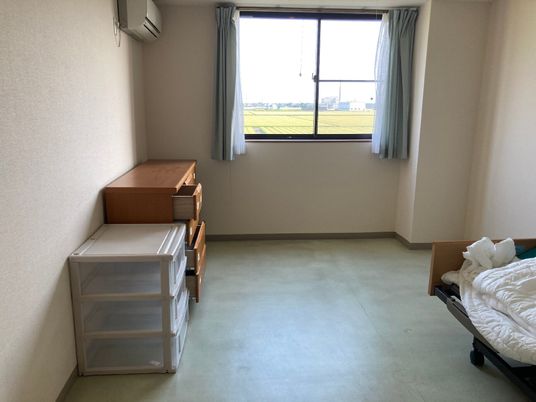 大きな窓の外には豊かな自然が広がっていて、寝具付きのベッドが置かれた部屋には収納ケースやタンス、エアコンがある。