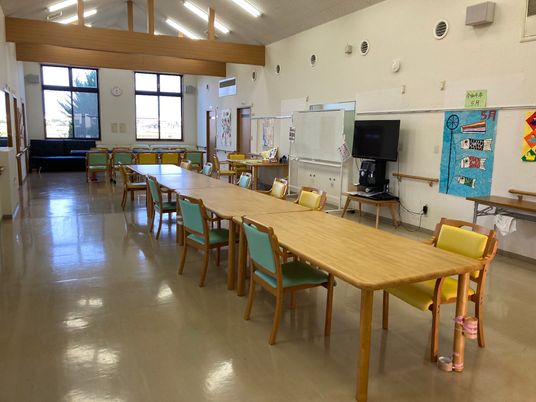 長細く大きな木製のダイニングテーブルセットが置かれ、テレビやホワイトボードもあり、天井が高い。