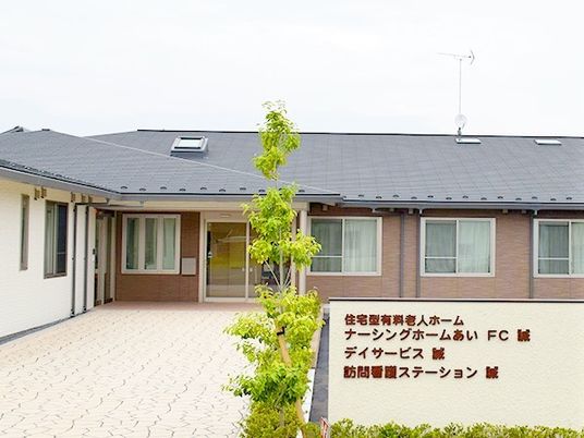 デイサービス・訪問看護など複数の施設名がある看板とその奥にある建物の外観写真