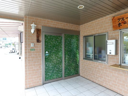 左右対称に設けられている扉のうち左側は、普段は閉鎖されており出入りには使っていない。緑色のシートが貼られている。