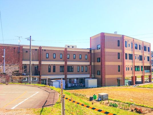 高齢女性が薬を飲もうとしているところを見守る若い女性スタッフ。笑顔でコップを持っている。
