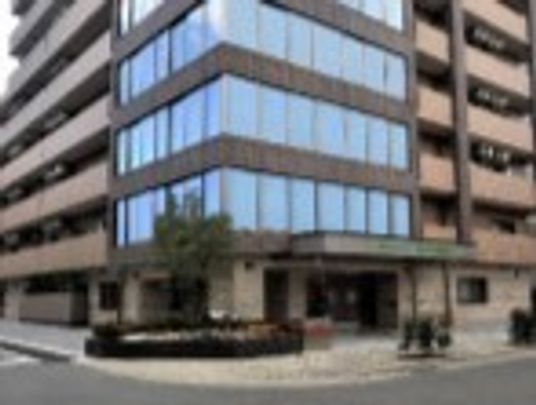 ブラウン系の９階建ての建物は各フロアにベランダがあり、玄関先には車寄せが付き、大きな木も植えられている。