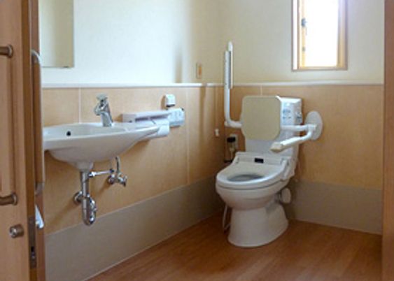両サイドに手すり設置されたトイレには背もたれもあり、手洗い場も備わっている。