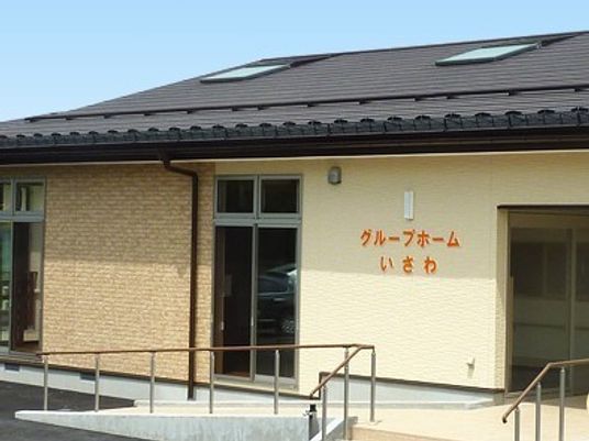 平屋建ての建物には瓦屋根が付き、玄関のには階段とスロープがある。アットホームな雰囲気。