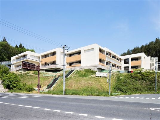 白とベージュの大きな建物は各フロアにベランダが付き、周辺を自然に囲まれている。