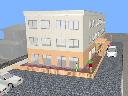 3階建ての建物。ベージュと白で周辺には住宅がある落ち着いた環境。花壇に花が植えられている。