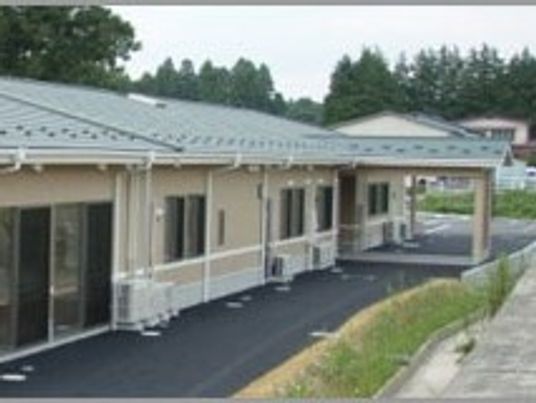 グリーンの屋根が付いた平屋建ての建物の玄関先には車寄せが付いている。緑に囲まれた立地。