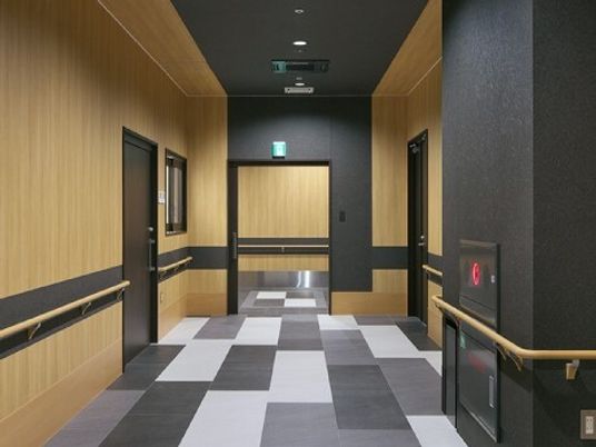 モノクロのモザイク柄のフロアのエントランス。壁には木製の手すりが付いていて、防災設備も設置されている。