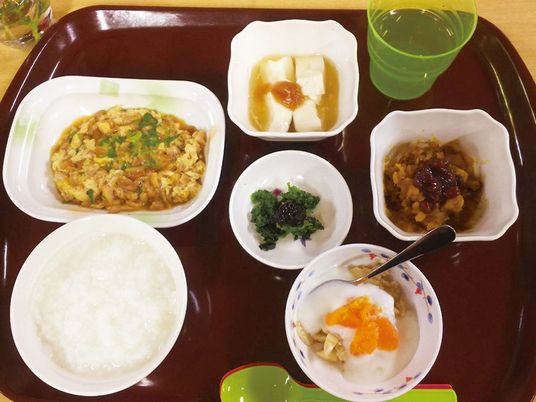おかゆや卵料理、豆腐、青菜の和え物などが並んだブラウンのトレー。
