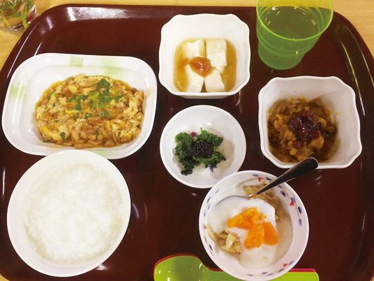 おかゆや卵料理、豆腐、青菜の和え物などが並んだブラウンのトレー。