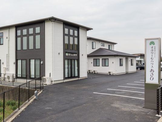 白と黒の2階建ての建物が広い駐車場付きの敷地内に建っていて、出入り口には看板もたてられている。