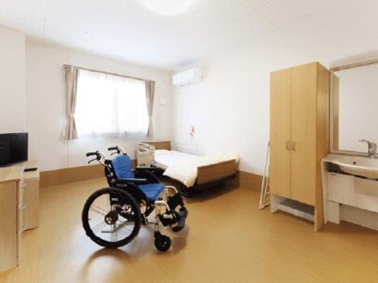車いすとベッド、テレビなどが置いてあるワンルームタイプの部屋