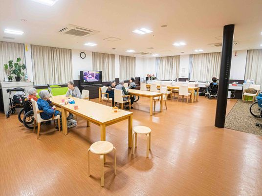 リビングダイニングには木製のテーブルセットが複数置かれ、入居者が思い思いの場所にいる。