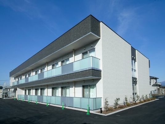 白い外壁の２階建ての建物は日当たり良好で各フロアにベランダがあり、草木も植えられている。