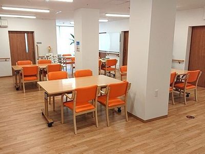 オレンジの椅子がセットされたダイニングテーブルが置かれたフローリングの共有スペースには白い花や観葉植物が飾られている。