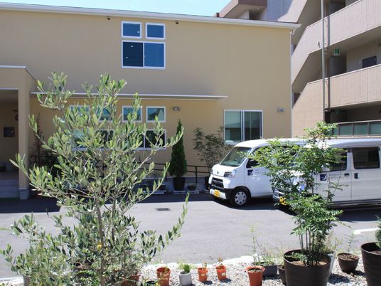 日当たりのいい場所に建っている２階建ての建物の前には駐車場があり、菜園スペースもある。