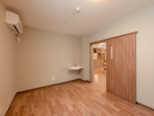 エアコンと洗面台がついた小さなワンルームタイプの部屋。市背うt内の居室の様子