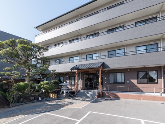 4階建ての建物。手すり付きのスロープがあり、日本庭園や駐車スペースもある。