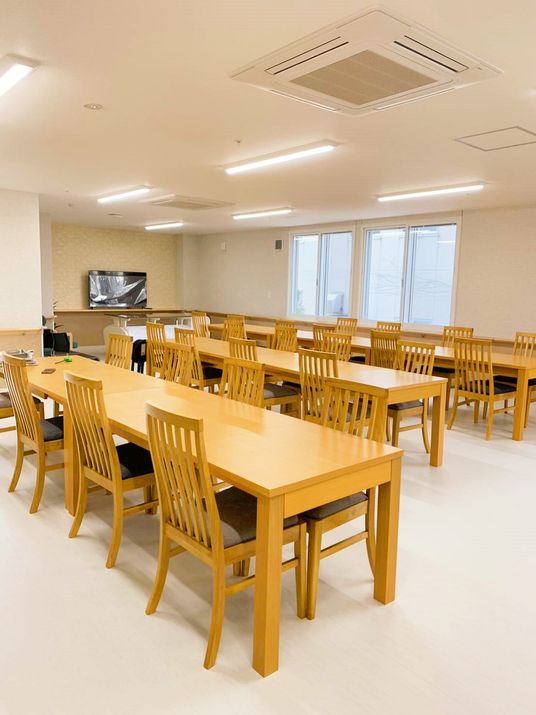 ベージュの机と茶色の椅子のセットが複数ある食堂