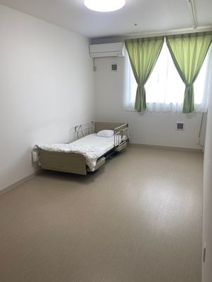 自然豊かな場所を車いすで散歩している高齢男性とそれを補助しながら話している女性スタッフ
