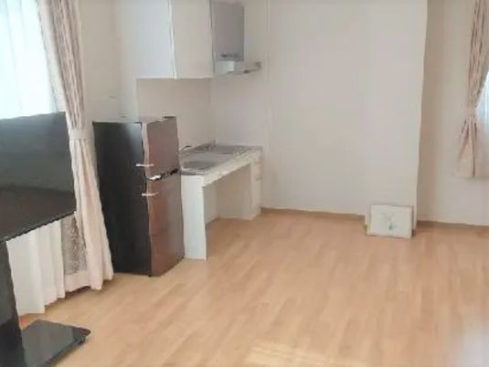 テレビや冷蔵庫が付いたフローリングの部屋には車いす対応のIHクッキングヒーター付きのキッチンがあり、カーテンが付いた窓もある。
