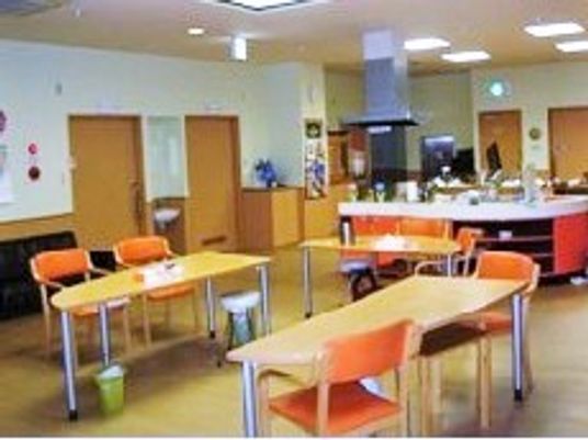 オレンジの椅子がセットされたダイニングテーブルが並び、本格的なキッチンがある共有スペース。