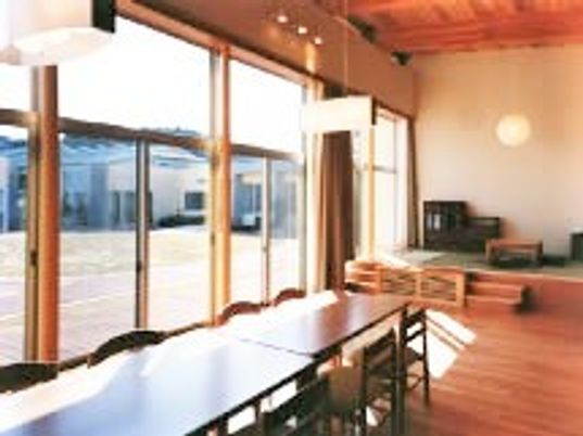 長机と椅子が並んでいる施設内のリビングの様子。日当たりの良い一面採光の窓