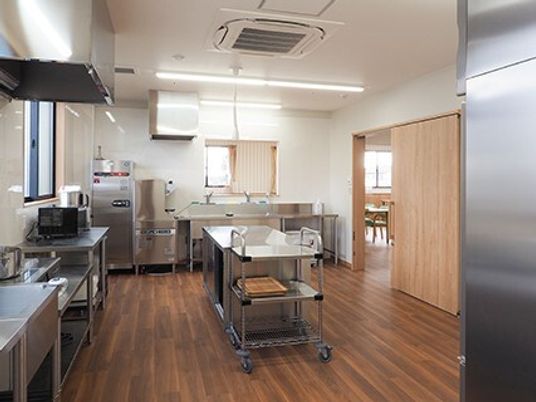 ステンレス製の調理器具がそろったフローリングの厨房には窓があり、ドアの奥には共有スペースがある。