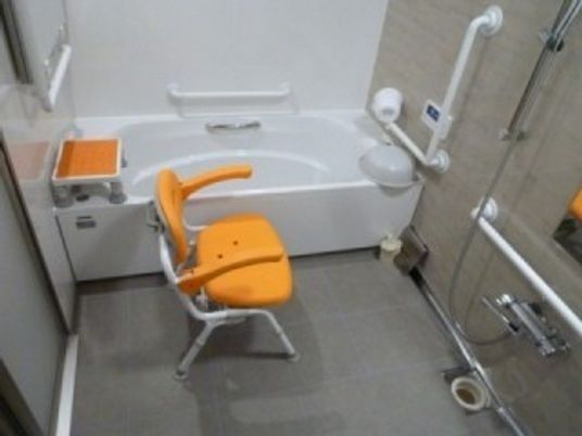 オレンジのシャワーチェアや手すりが設置された一人用の浴槽がある浴室。明るい雰囲気。