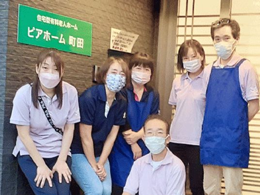 ポロシャツを着た男女のスタッフがホームの玄関前に集合している様子。