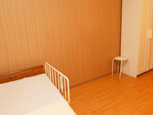 介護ベッドやスツール、クローゼットが置かれている段差のないフローリングの部屋。