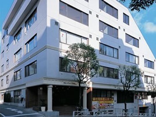 白を基調とした大きな建物にはたくさんの窓があり、建物の周りには草木が植えられ、地下の階もある。