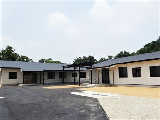 広めの敷地内に駐車場と建物がある様子。山に囲まれた小さな建物