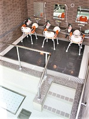 シャワーチェアが３脚並ぶ施設内の浴室。手前に手すり付きの浴槽がある