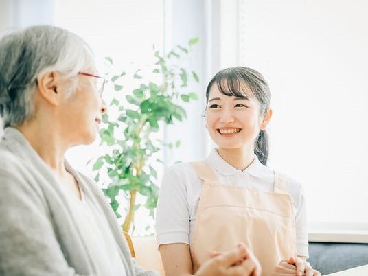 エプロンを付けた若い女性スタッフとカーディガンを着た高齢女性が笑顔で話している。