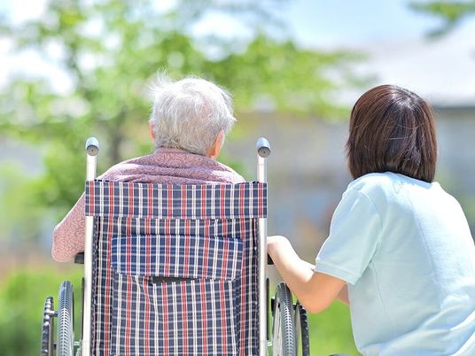 車いすの高齢女性と付き添いの若い女性スタッフが一緒に屋外で過ごしている。