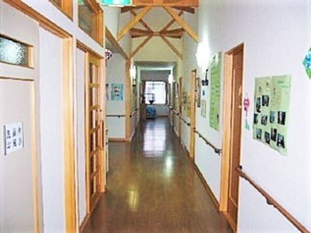 両サイドに手すりがあるまっすぐな廊下には居室のドアが並び、突き当りには大きな窓がある。 常に安心がそばにある環境をご用意！状況に応じた医療・看護・介護サービスを個別にご提供いたします。