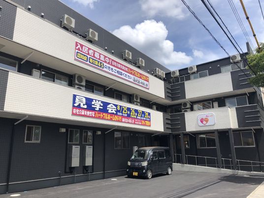 ダークグレーの3階建ての建物はエル字型で日当たりのいい場所にあり、駐車スペースもある。