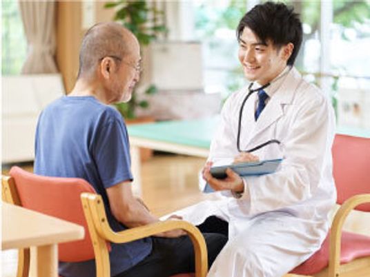 カルテのようなものを見ながら話している白衣を着た男性スタッフと眼鏡をかけた高齢男性。