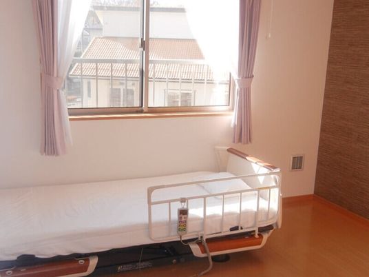 介護ベッドが置かれている部屋にはレースカーテンとカーテンが付いた大きな窓があり、明るい雰囲気。