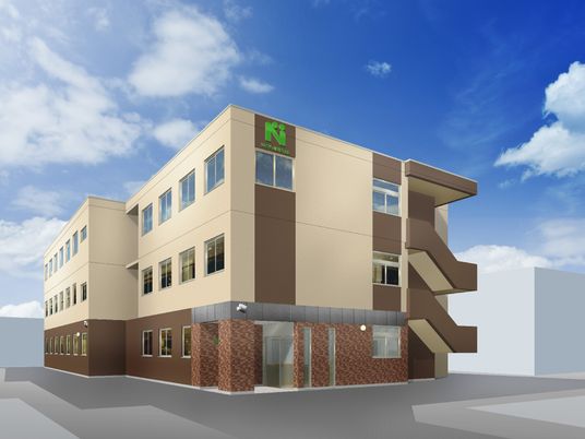 白とベージュの3階建ての建物の側面には屋外階段も設置され、外壁にはエヌの文字が書かれている。