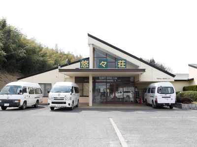 平屋建ての建物。手すり付きのスロープが付き、広い駐車スペースがある。
