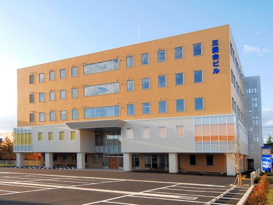 オレンジをメインとした外観で外壁にはブルーの文字で住宅名が書かれている。敷地内には駐車場がある。